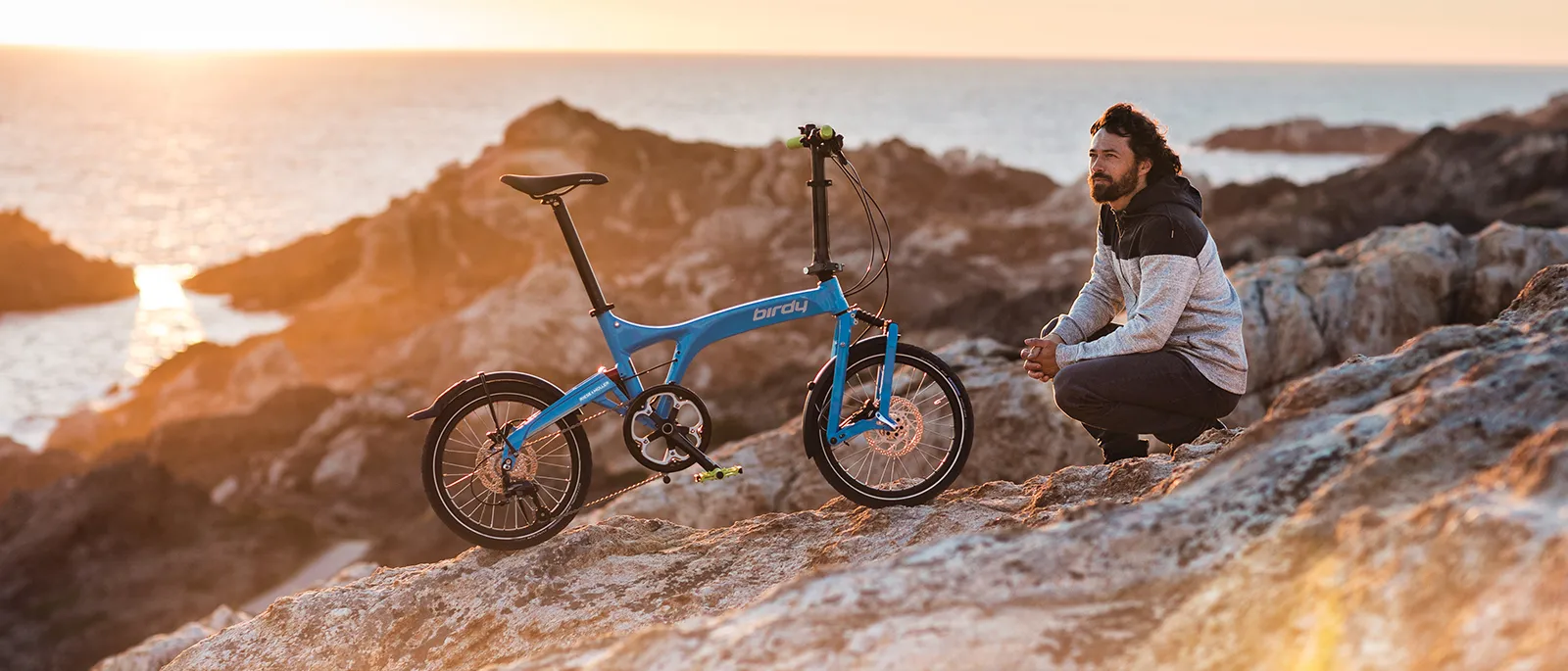 A sunset coastal scene with a man and his Birdy folding bike.