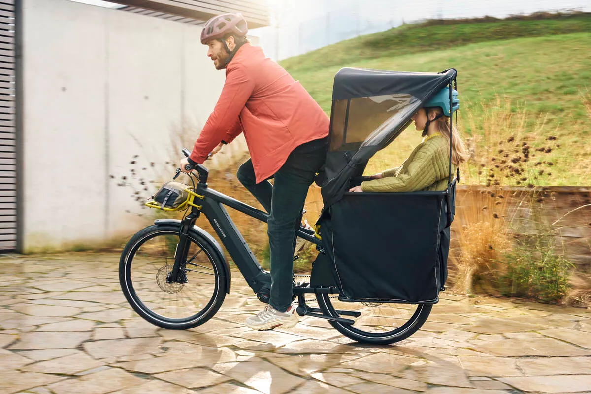 Person transporting passenger on Multicharger2 with weatherproof cargo carrier on bike path.