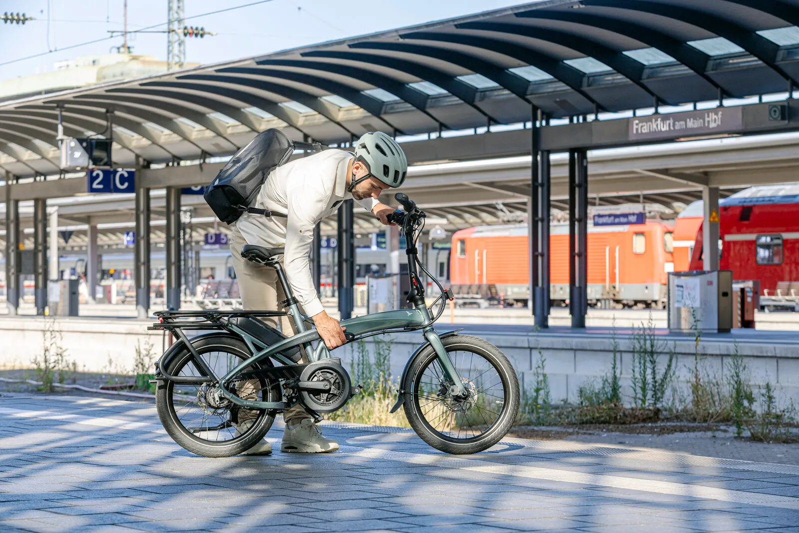 A commuter folding the Tern Vektron in urban verdant on a station platform.