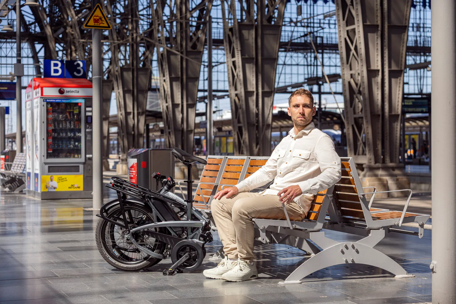 A commuter on a station bench with the folded Vektron in cosmic black beside him.