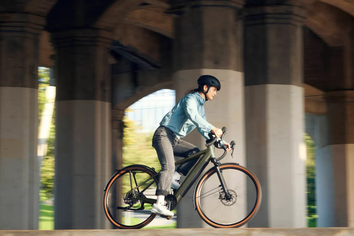 Cyclist riding a UBN Five commute with tan sidewall tyres under stone archway, wearing helmet and blue jacket.