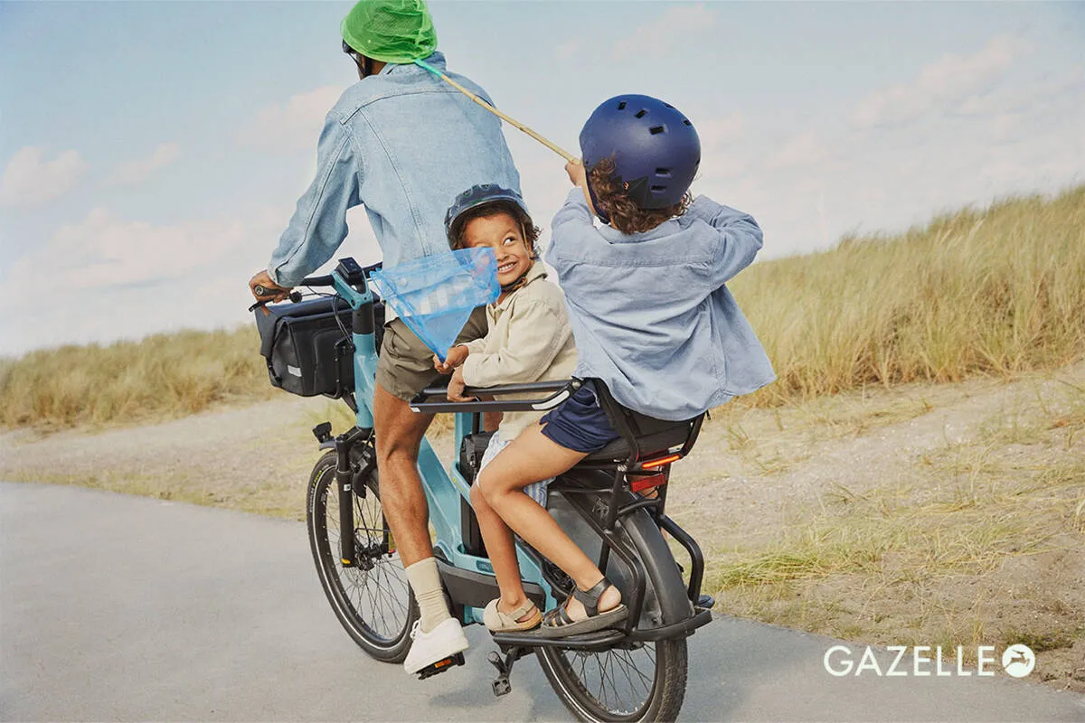 Family riding Gazelle Cabby e-bike along coastal path, two children sitting on extended rear carrier