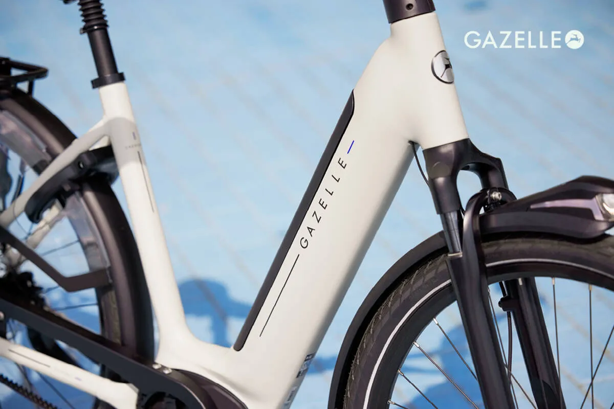 Close-up of ivory white Gazelle Grenoble C5 e-bike frame showing brand name and sleek tube design.