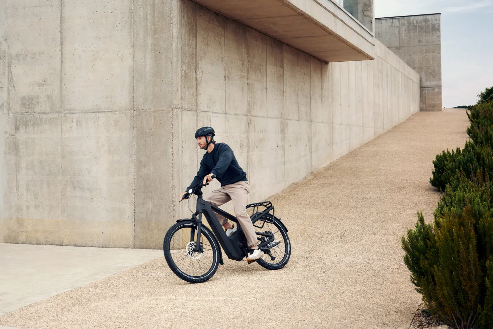 Man riding Riese & Müller Delite5 in stone grey past modern concrete architecture.