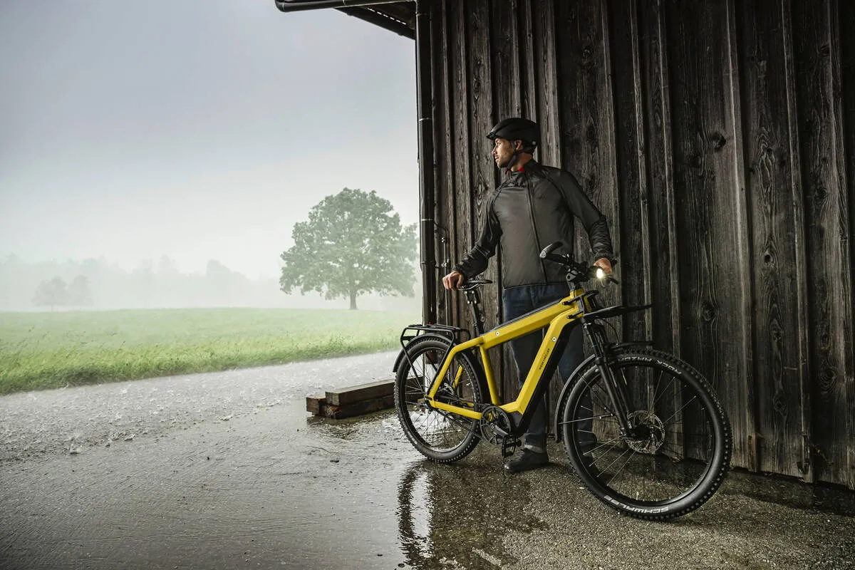 Cyclist sheltering with curry matt Supercharger by wooden barn on misty morning.