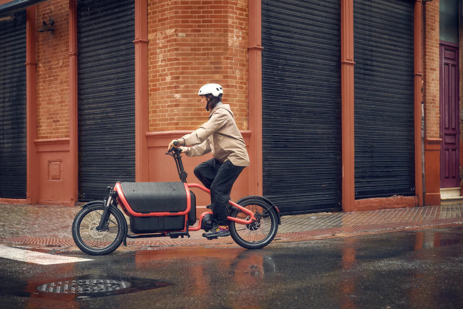 Rider cycling the Carrie2 vario in coral along a wet city street, showing the bike in full profile with Flex Box closed.