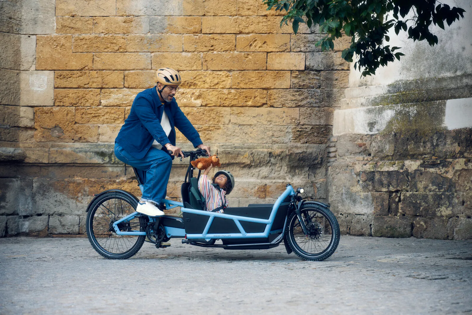 Rider cycling the Load5 75 vario in arctic with a child in the cargo box, passing a stone wall on a sunny day.