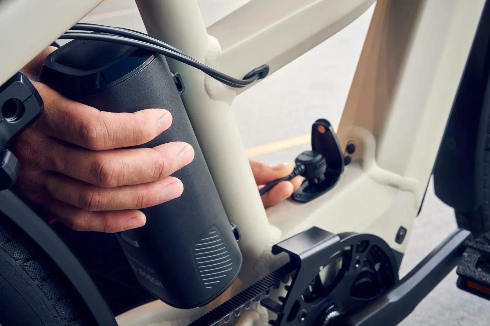 Close-up of the Multicharger3 DualBattery system, showing a hand removing a Bosch battery from the frame.