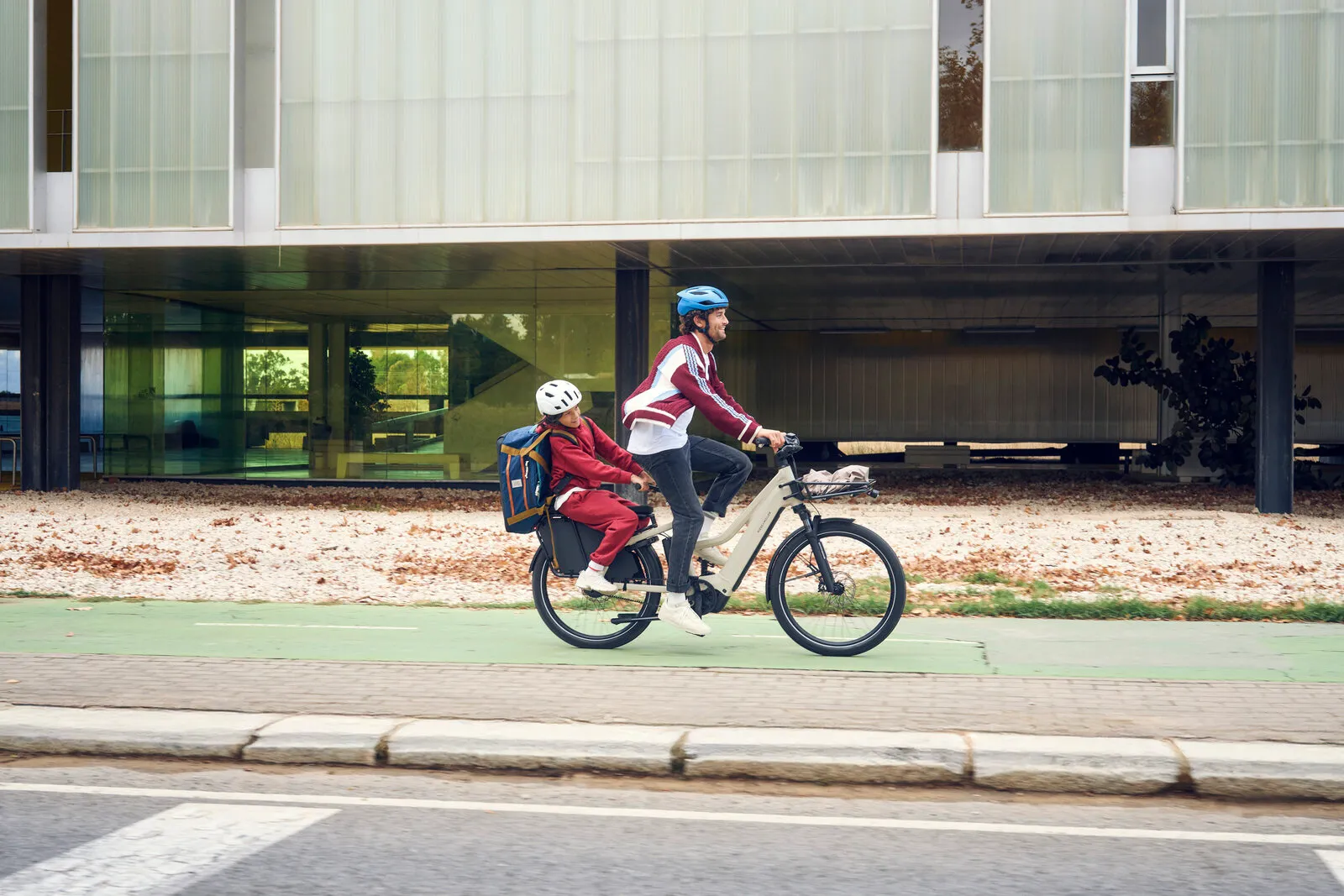 Rider cycling the Multicharger3 Mixte vario in desert/black with a child on the rear seat, full profile view on a cycle lane.