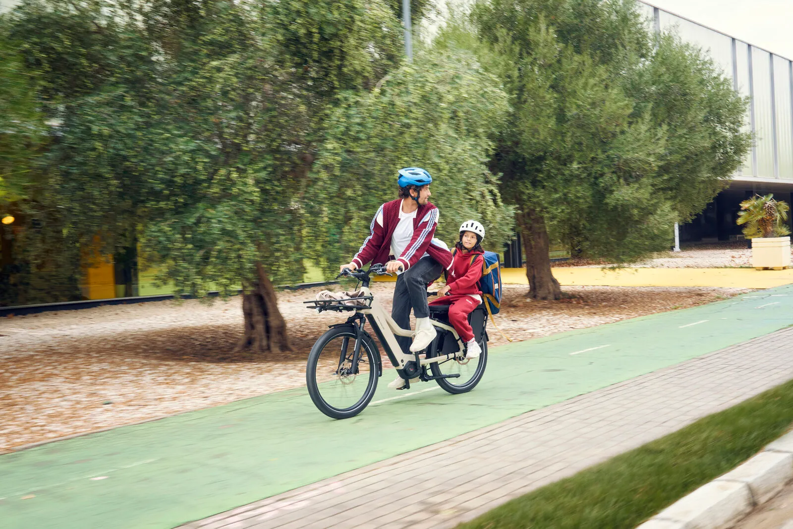Rider and child on the Multicharger3 Mixte vario in desert/black, cycling along a tree-lined cycle path.