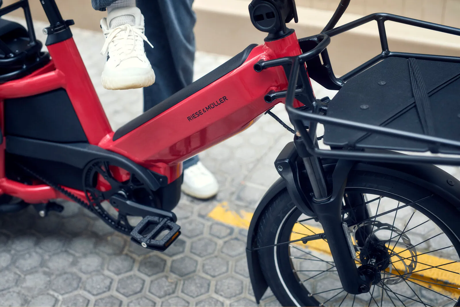 Close-up of the Multitinker2 low step-through frame in lava/black, showing the Riese & Müller branding, integrated battery and front carrier.