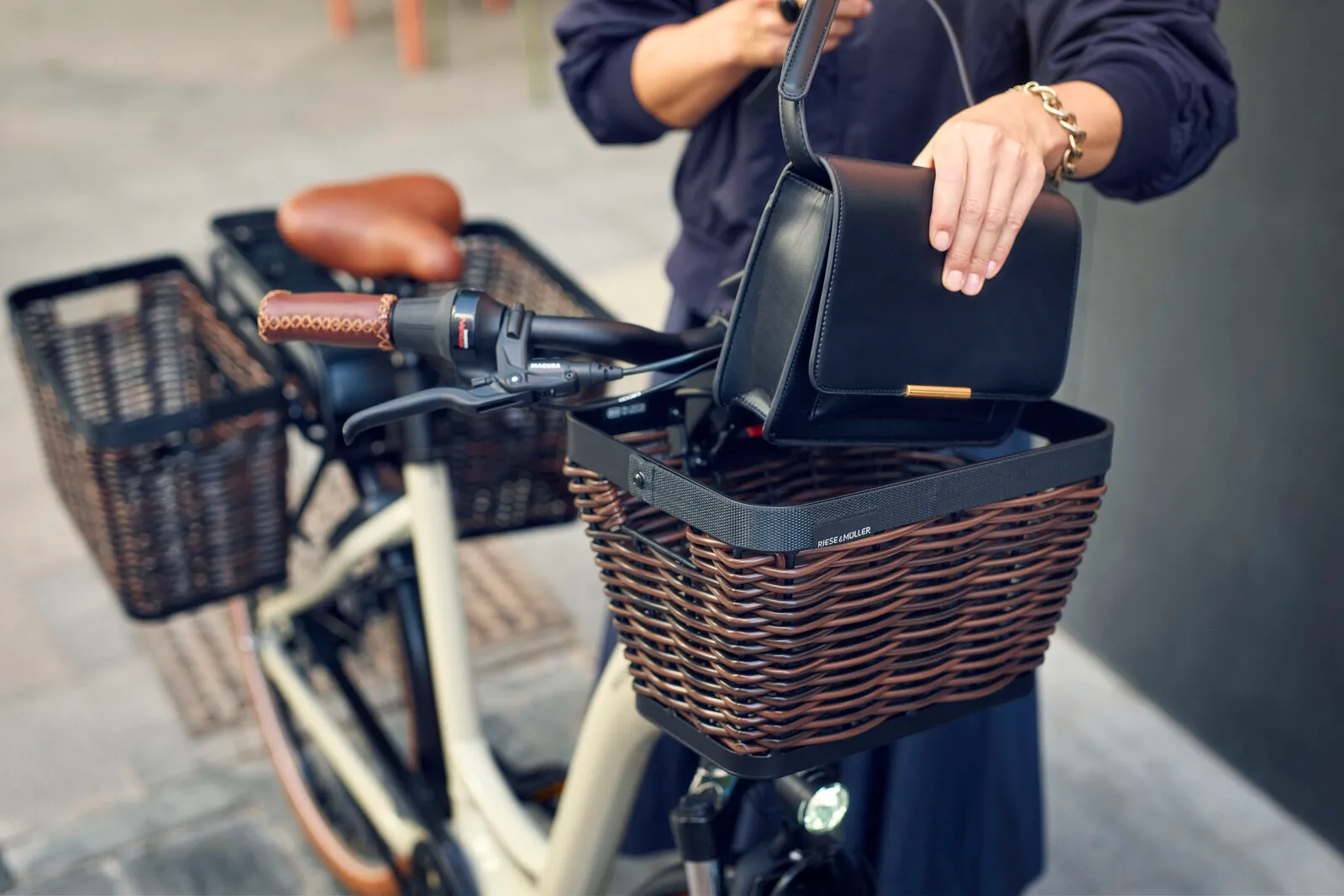 Close-up of the Swing5 front rattan basket with a handbag being placed inside, showing the leather grips and rear basket behind.
