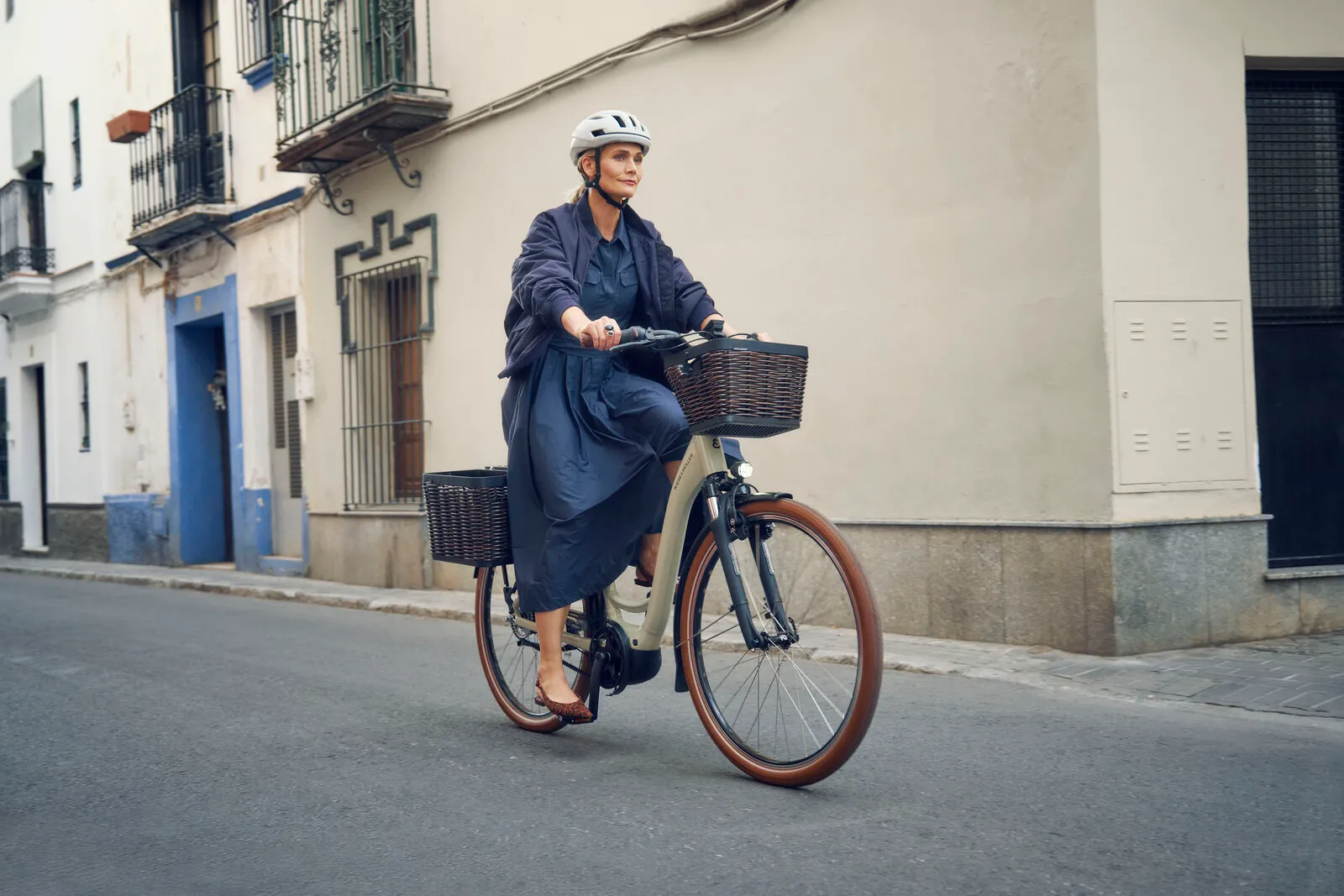 Rider cycling the Swing5 vario in almond with front and rear rattan baskets along a quiet city street.