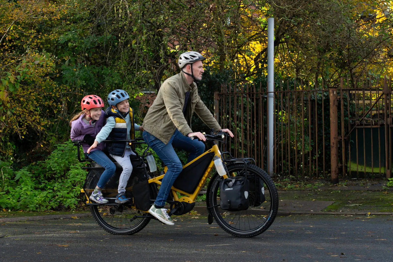 A man riding his Tern Orox along an urban street with two children on the back