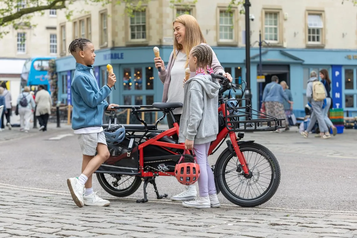 Family with red Tern Quick Haul Long e-bike in pedestrian square, woman and children holding ice creams beside the parked cargo bike