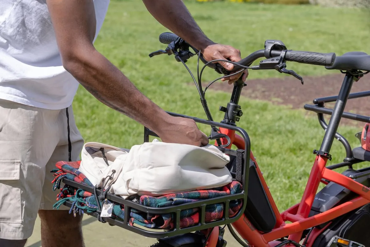 Close-up of hands loading fabric items into front basket of red Tern Quick Haul Long e-bike, showing cargo capacity and ease of access