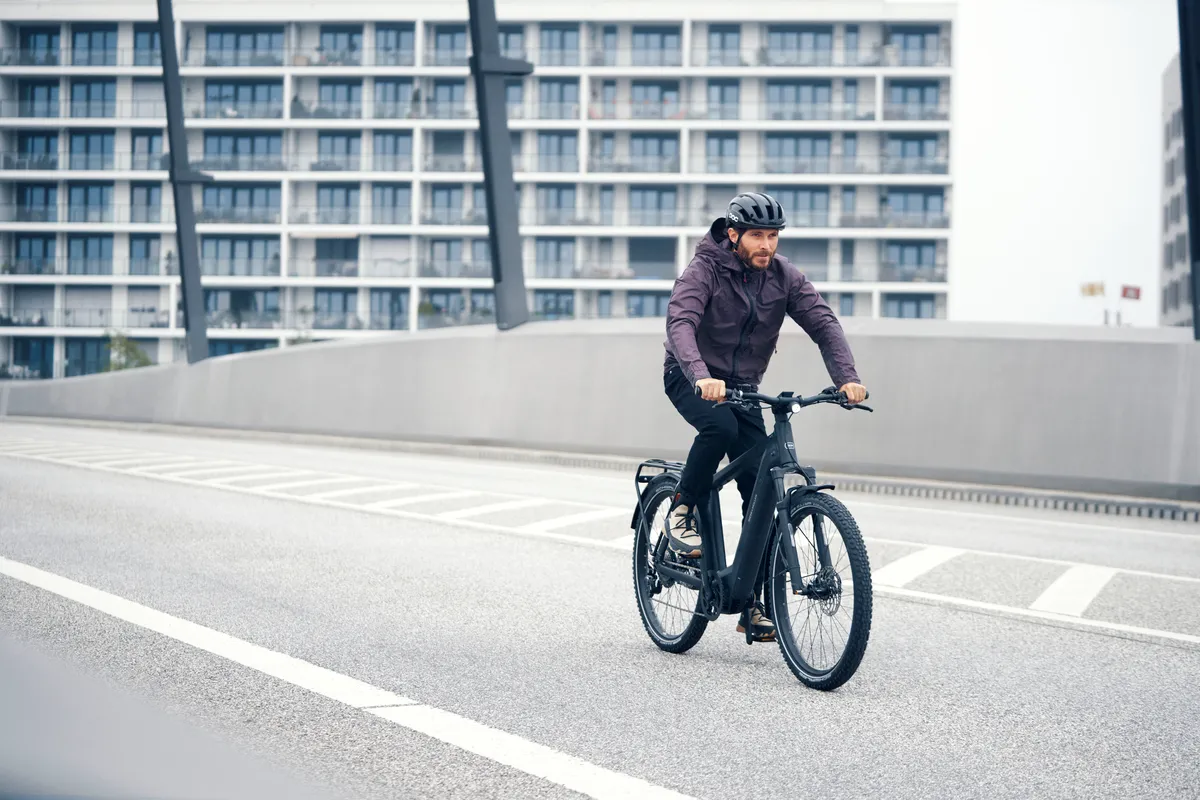 A man riding a black matt Riese & Müller Charger over a city bridge.