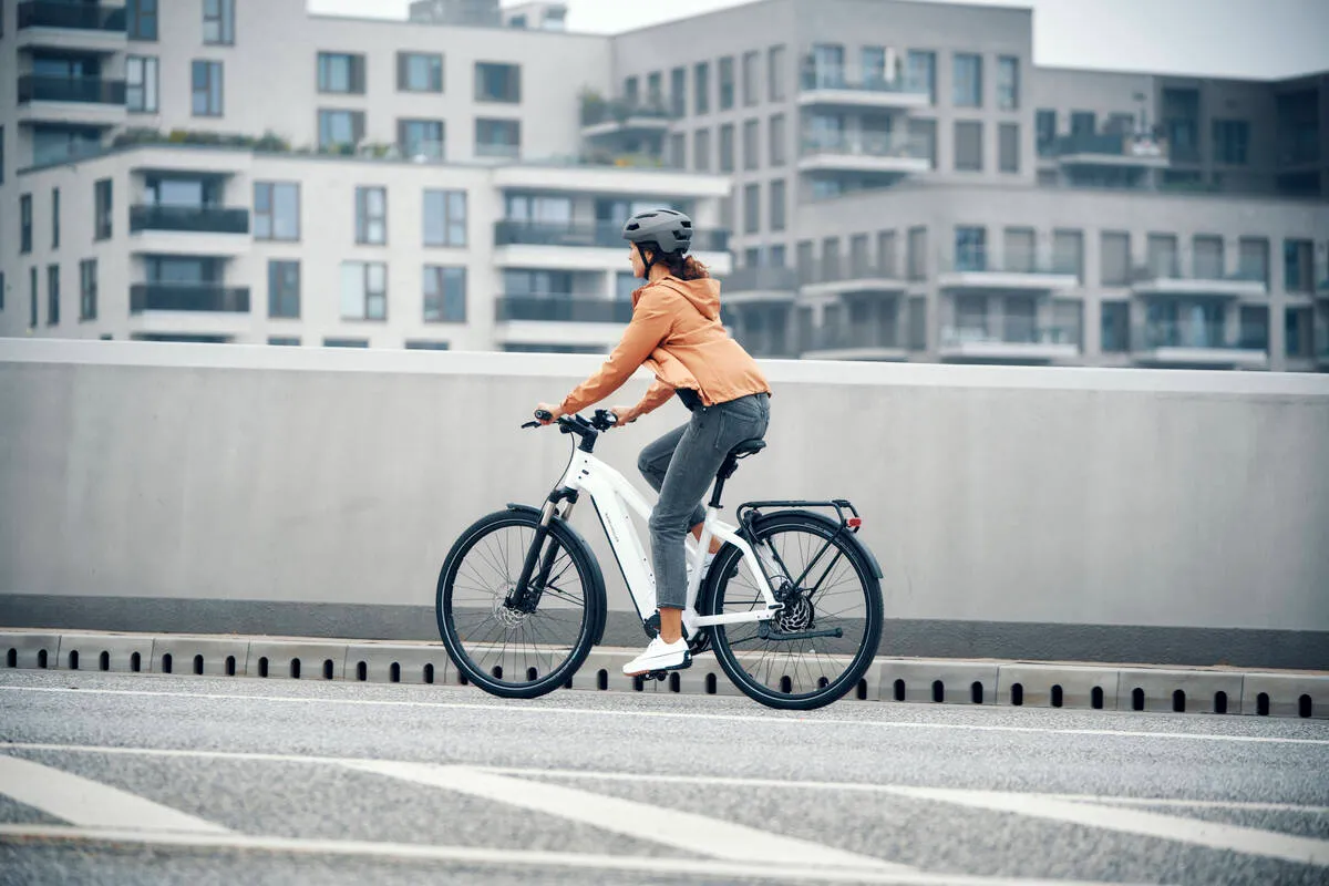 A lady riding a ceramic white Riese & Müller Charger over a city bridge.