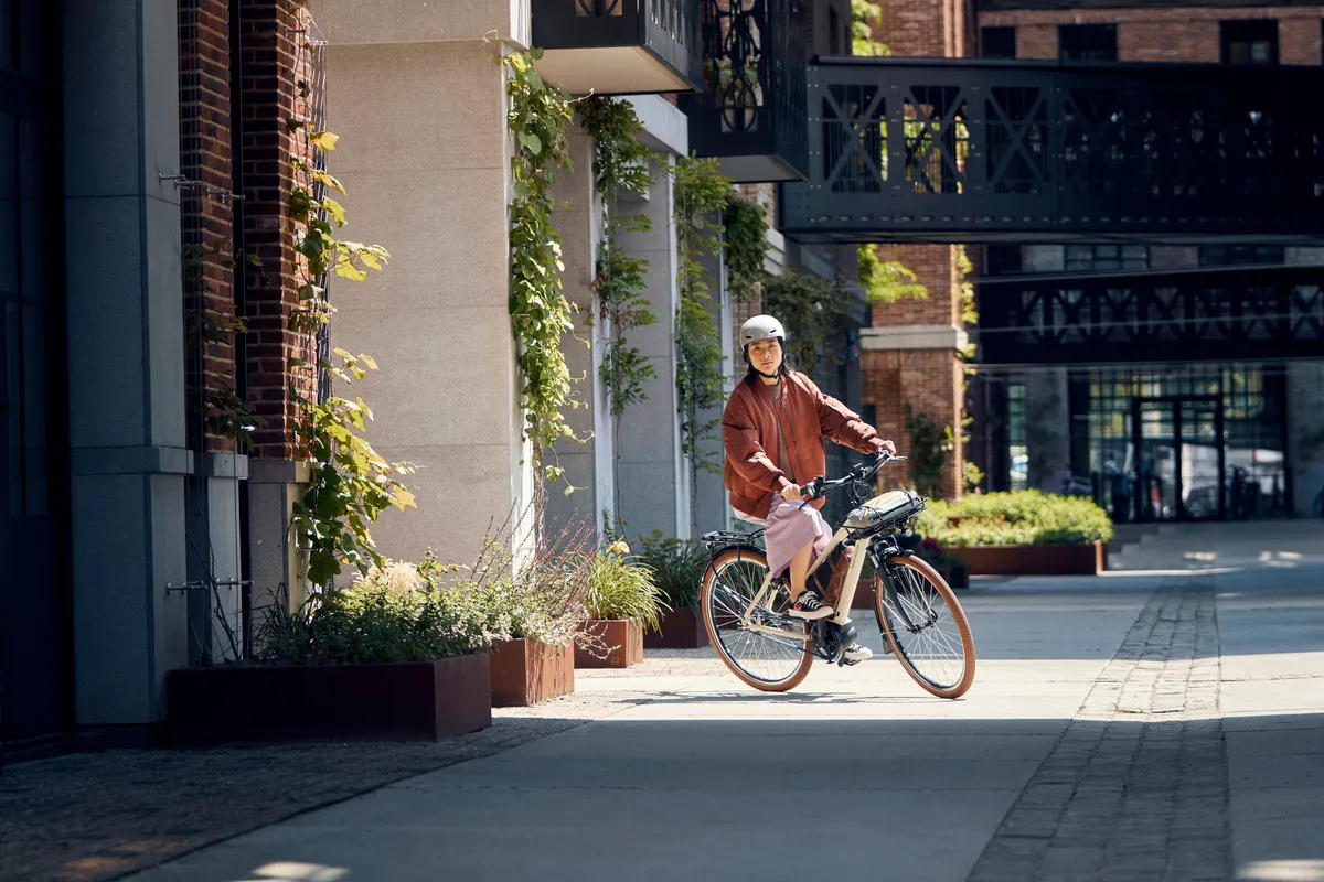 A lady riding a cream Riese & Müller Cruiser2 through a quiet urban street with lots of house plants.