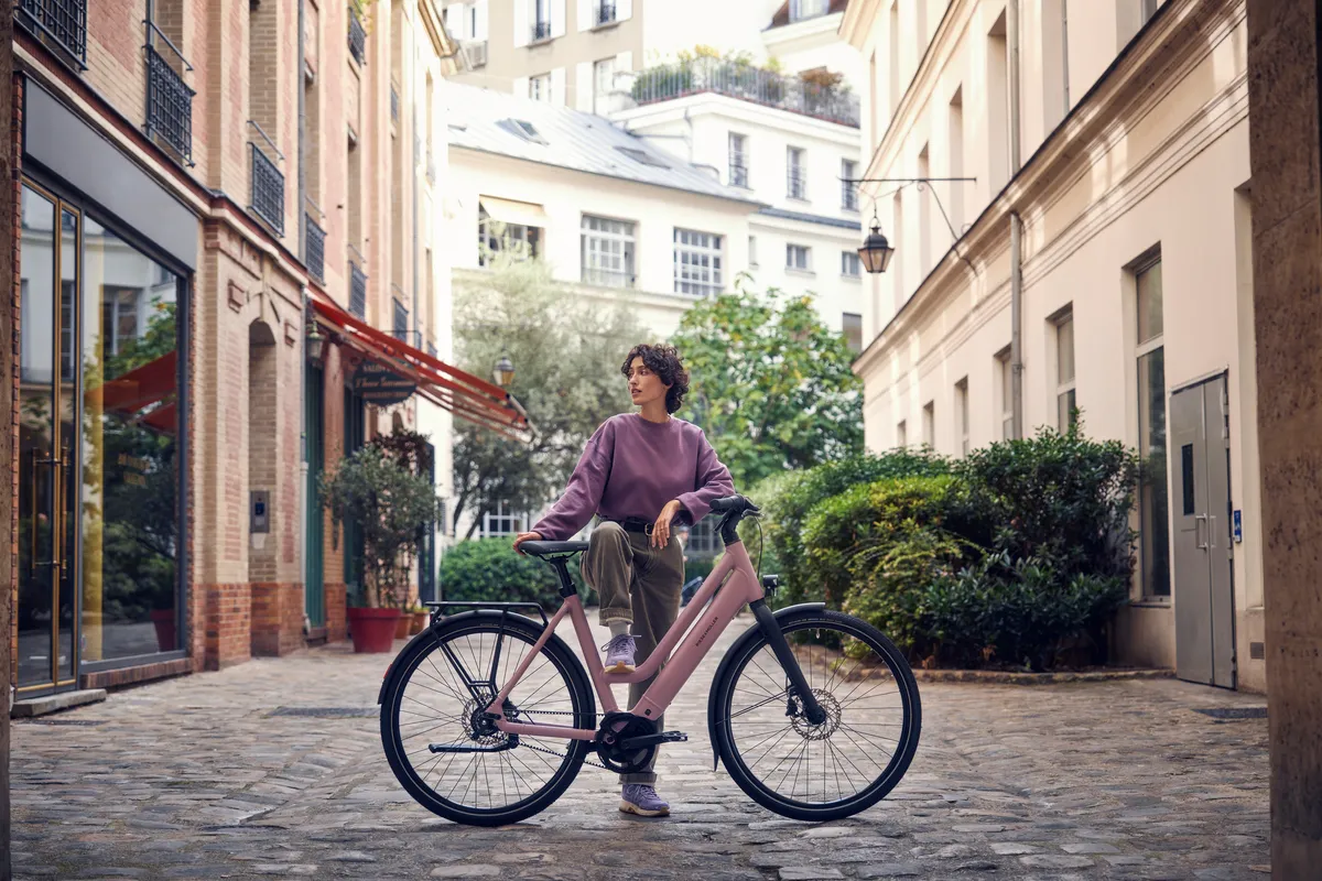 A lady with a Riese & Müller Culture electric bike. She stands astride the bike in a picturesque European street scene.