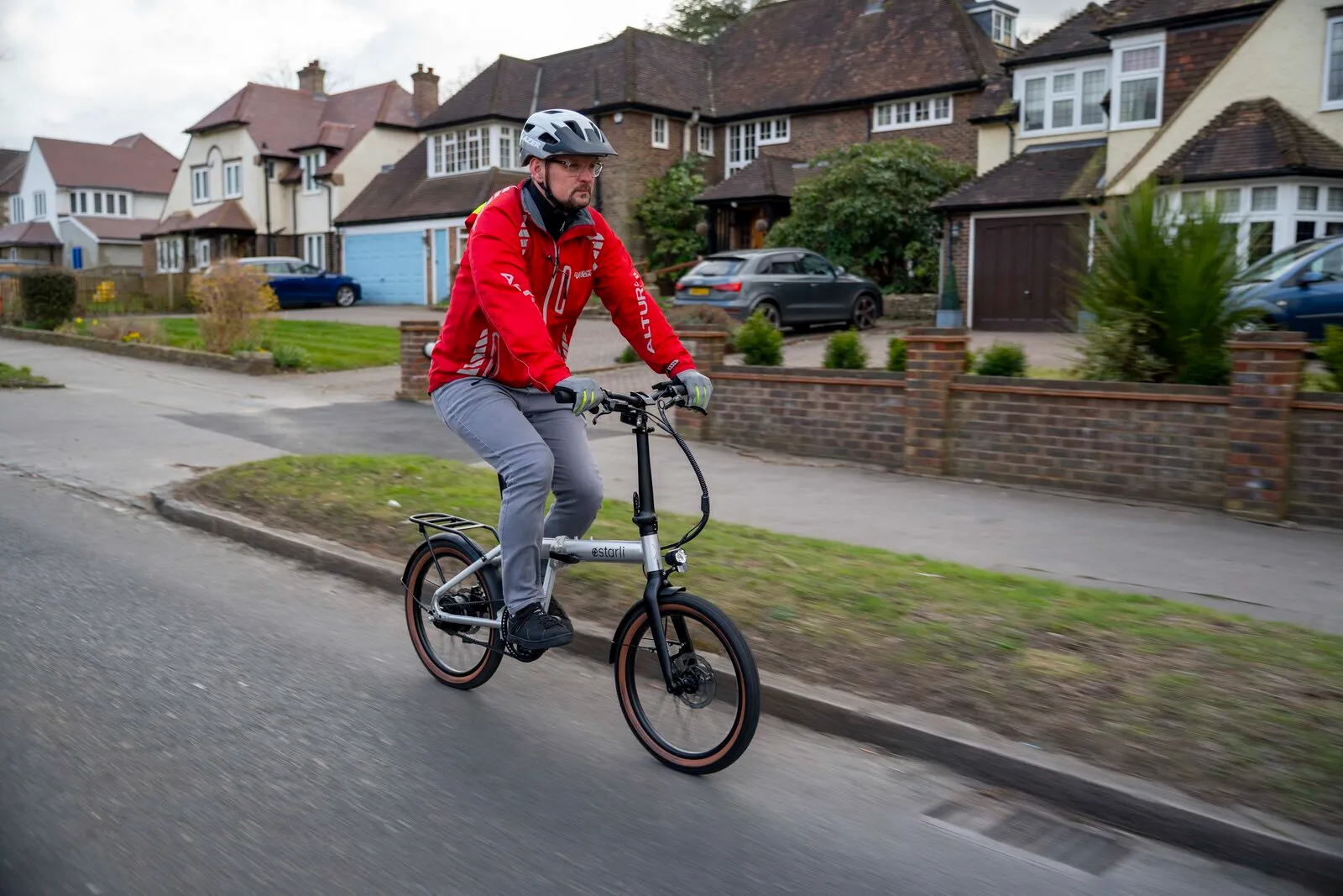 A cyclist in a red jacket riding the Estarli e20.X through a suburban neighbourhood.