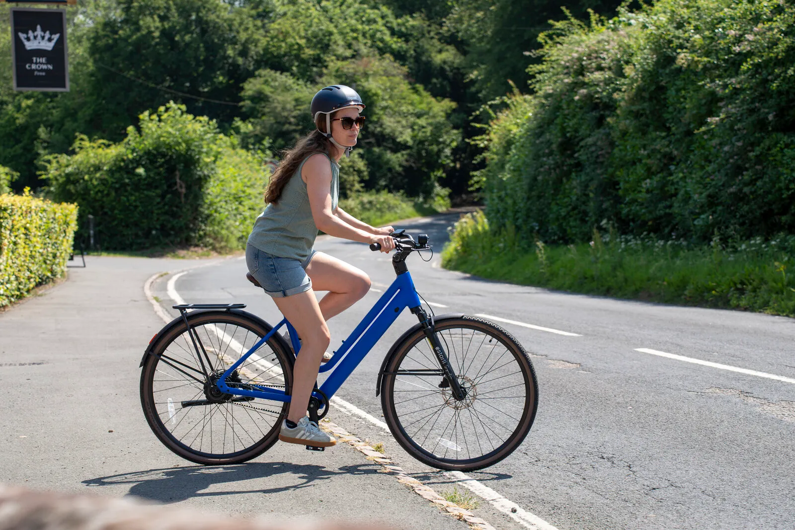 A woman riding the Estarli e28.X step-through in cobalt blue past a country pub.