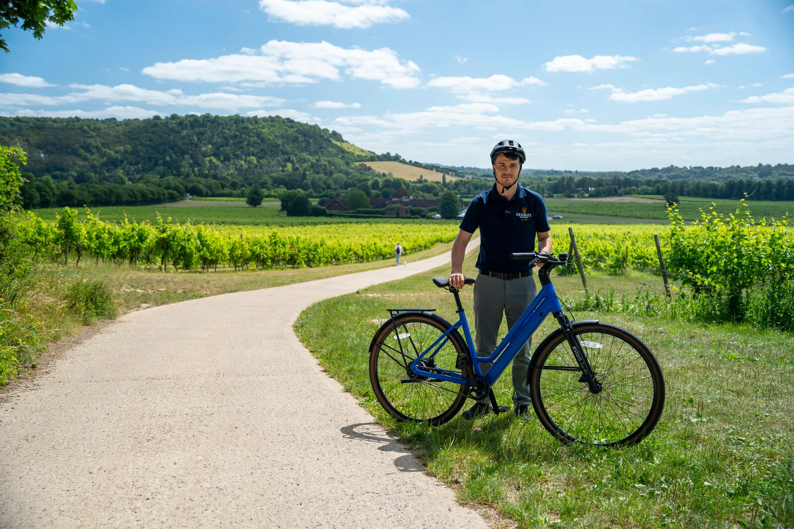 A man with the Estarli e28.X step-through in cobalt blue on a path through a Surrey Hills vineyard.