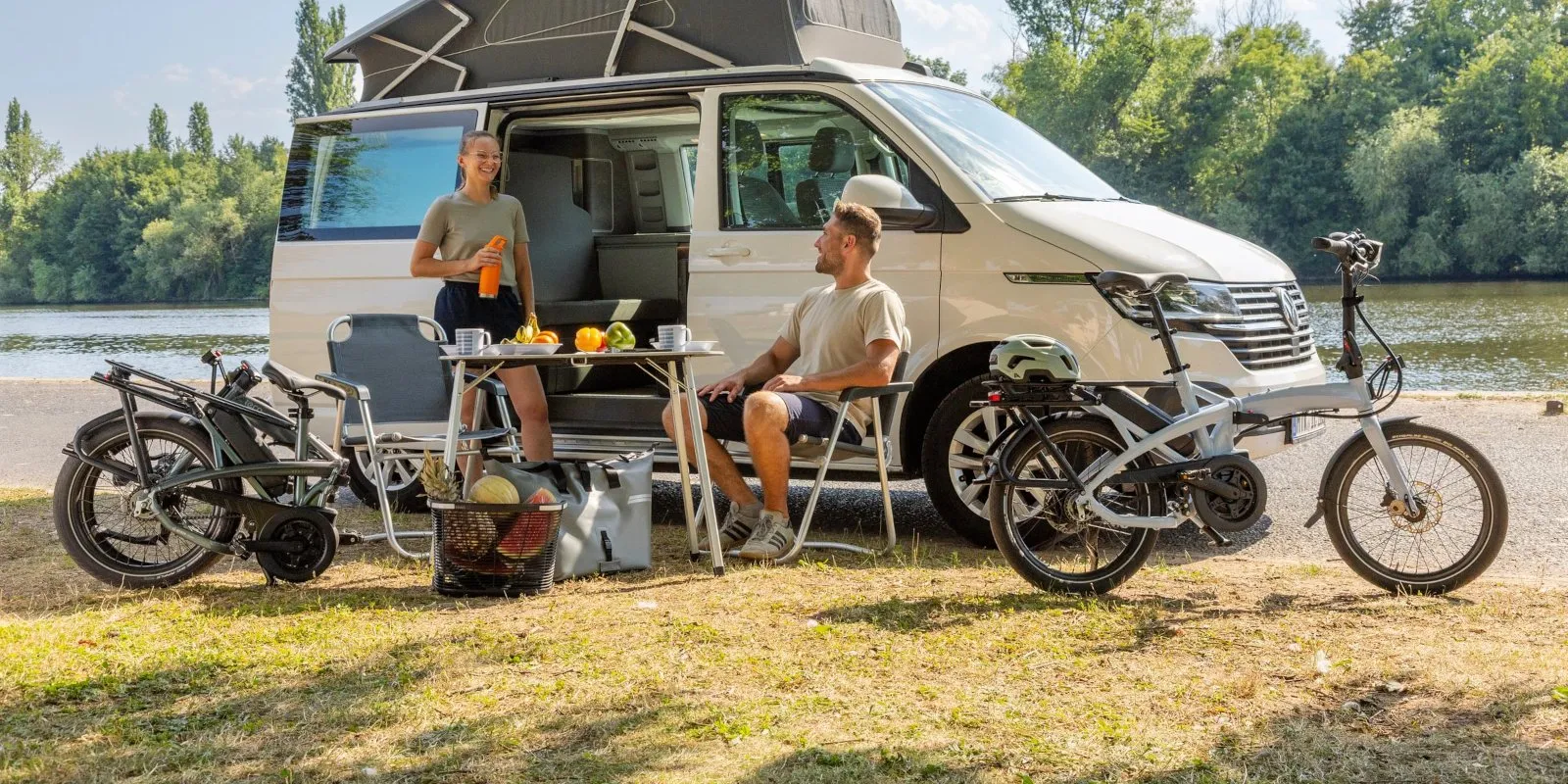 A couple relaxing by a campervan with two Tern Vektron folding e-bikes by a lake