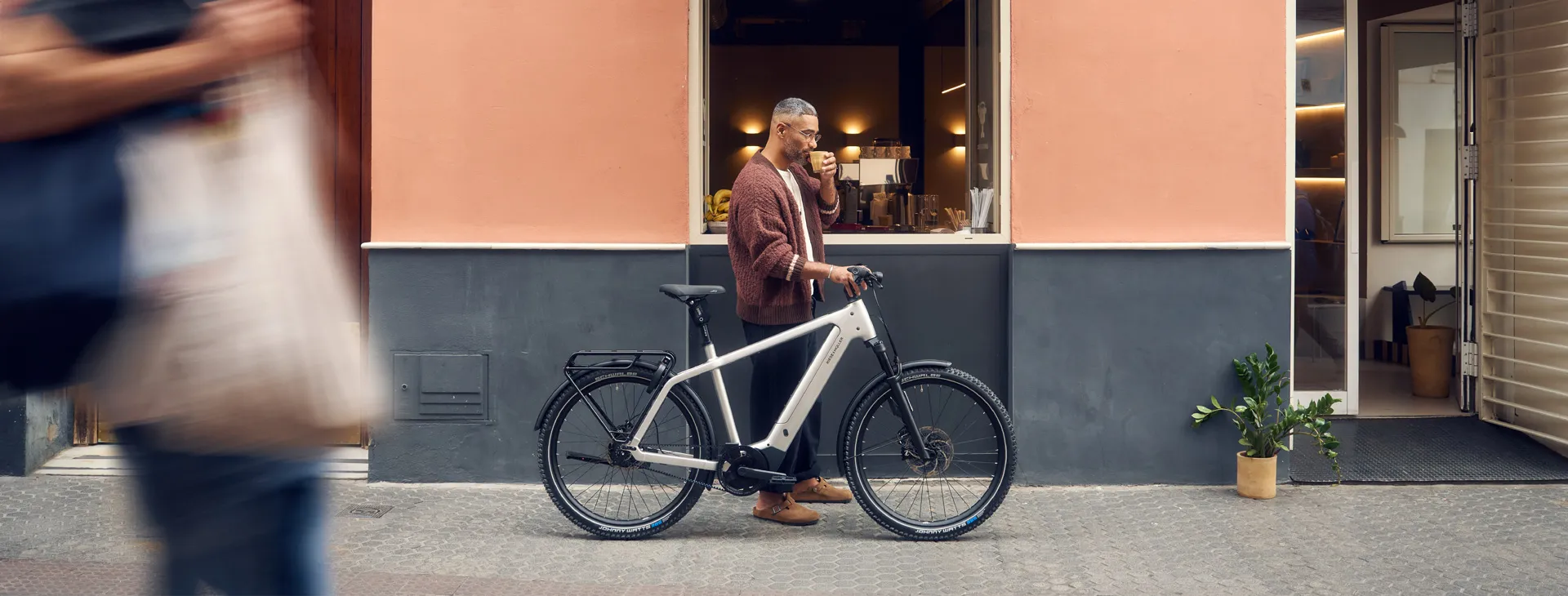 A man drinking coffee outside a café with a white Riese & Müller Charger