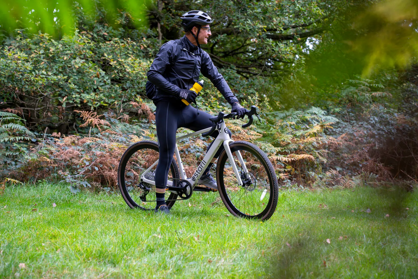 A rider pausing for a drink astride the lunar white G700 beside autumn ferns.