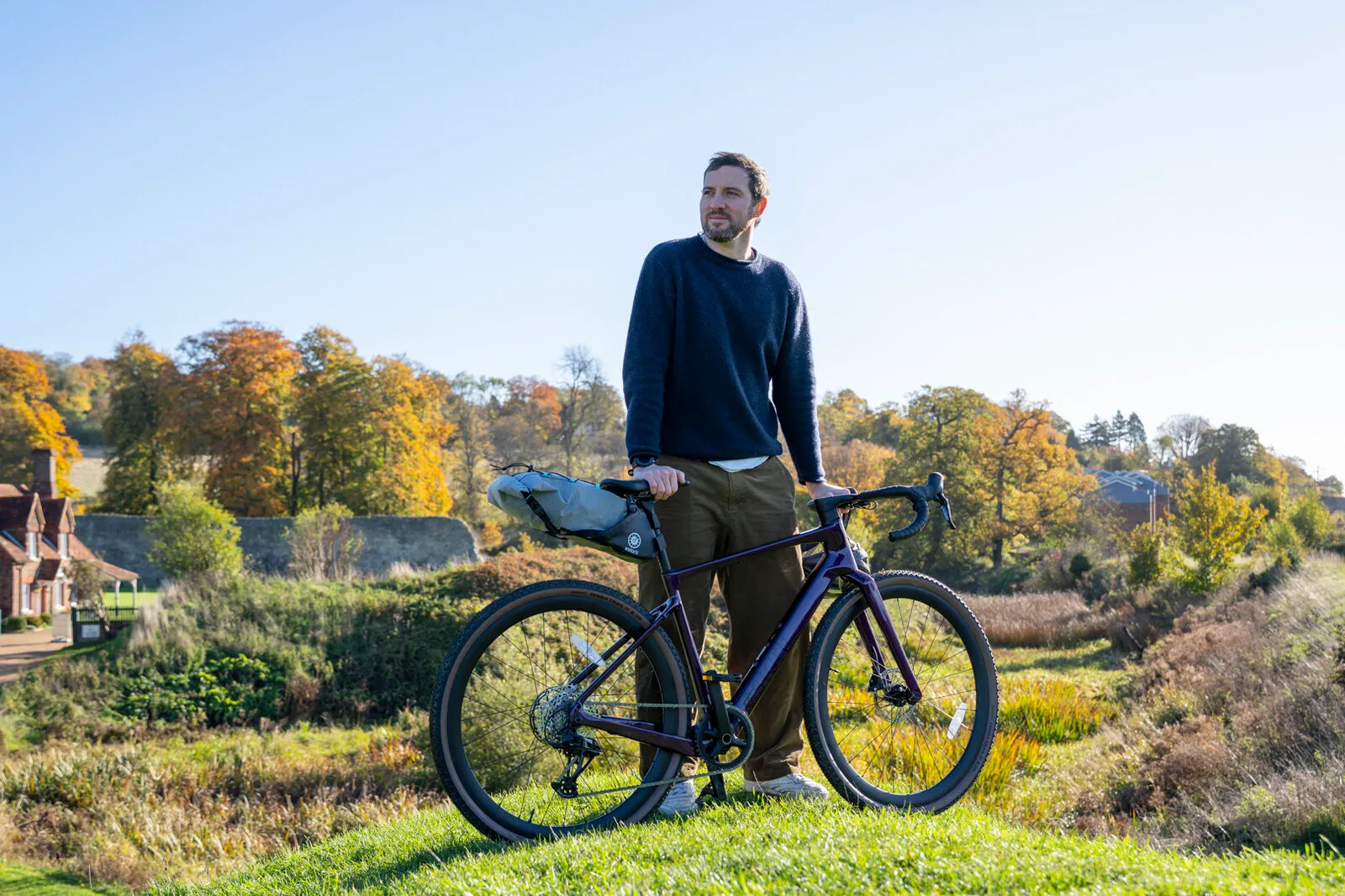 A man standing with a cosmic purple G700 and bikepacking seat pack above an autumn valley.