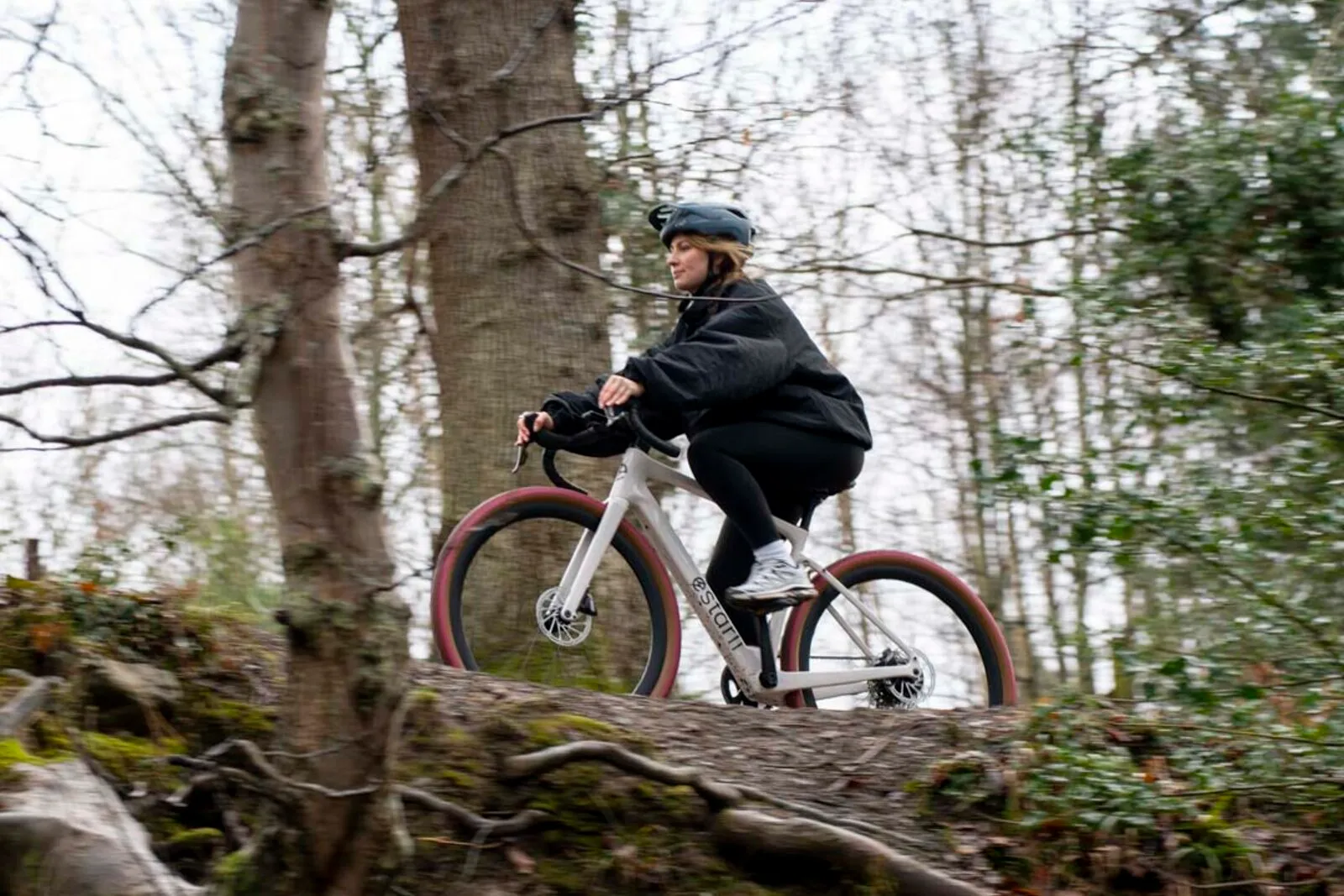 A woman riding the lunar white G700 through open woodland.