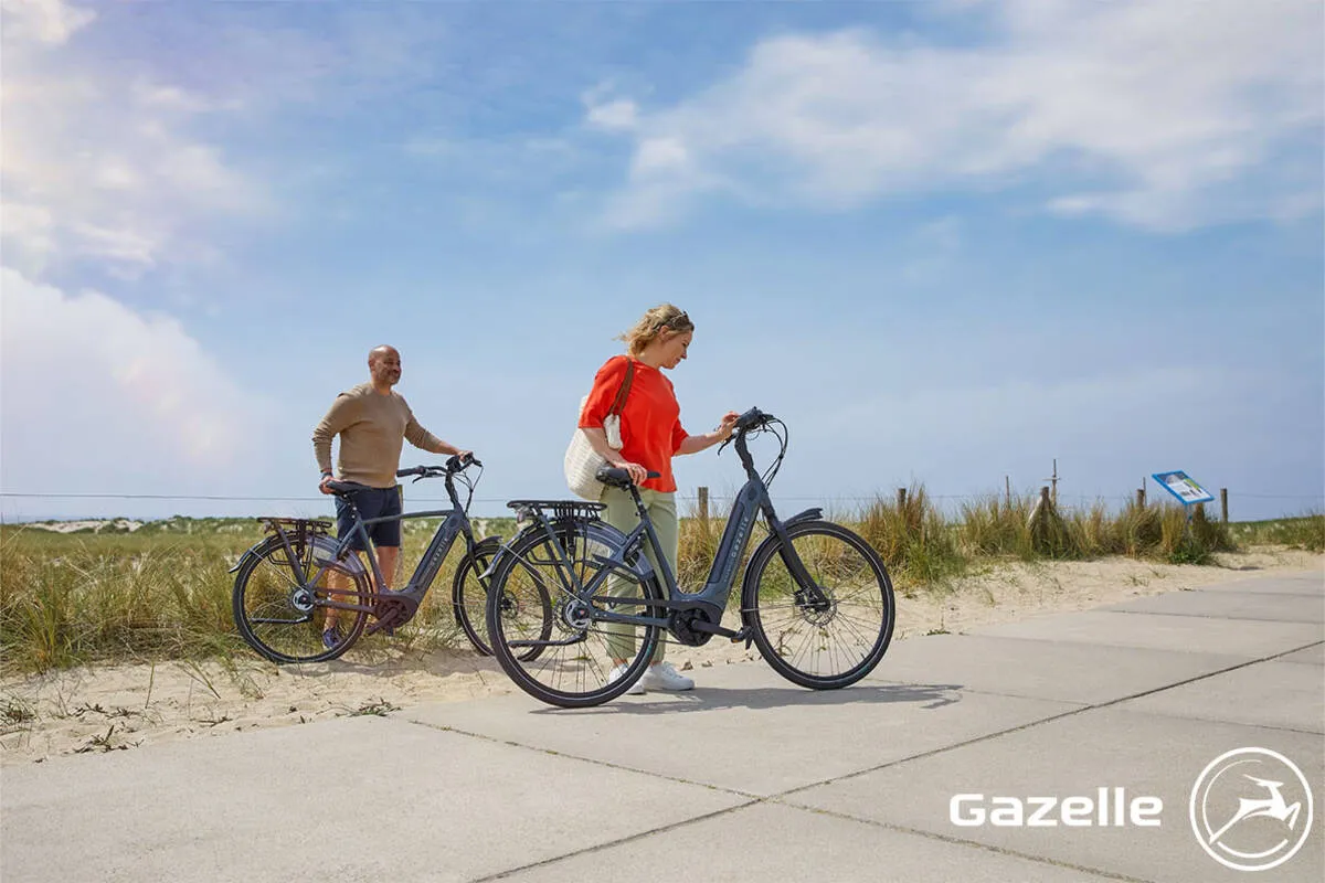 A couple taking a break on their Gazelle Grenoble bikes on a beachfront path.