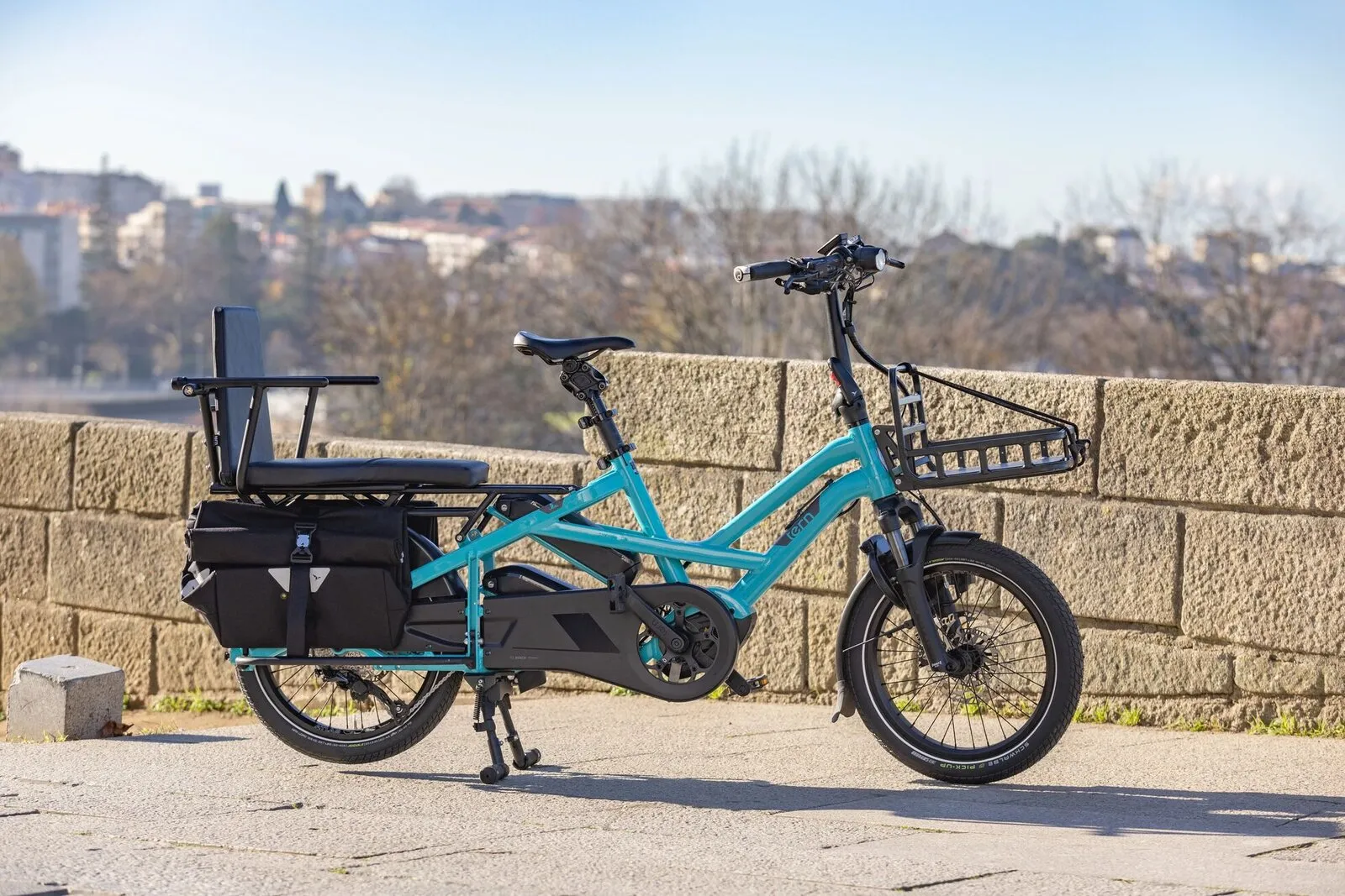 A beetle blue Tern GSD with a padded rear passenger seat and front Transporteur rack beside a stone sea wall.
