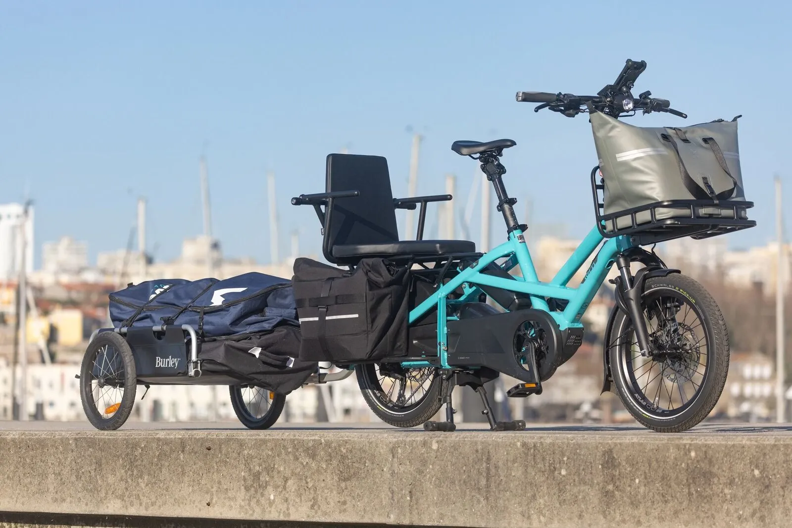 A beetle blue Tern GSD with a Captain's Chair passenger seat, panniers and a trailer at a harbour.
