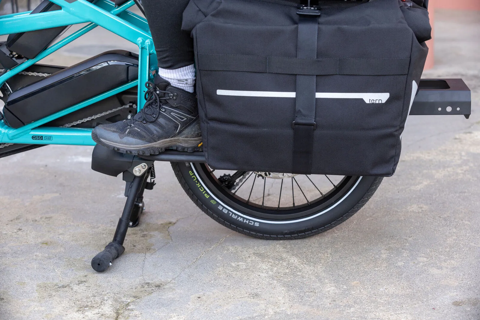 A passenger's foot resting on the rear deck of a beetle blue Tern GSD beside a Tern pannier.