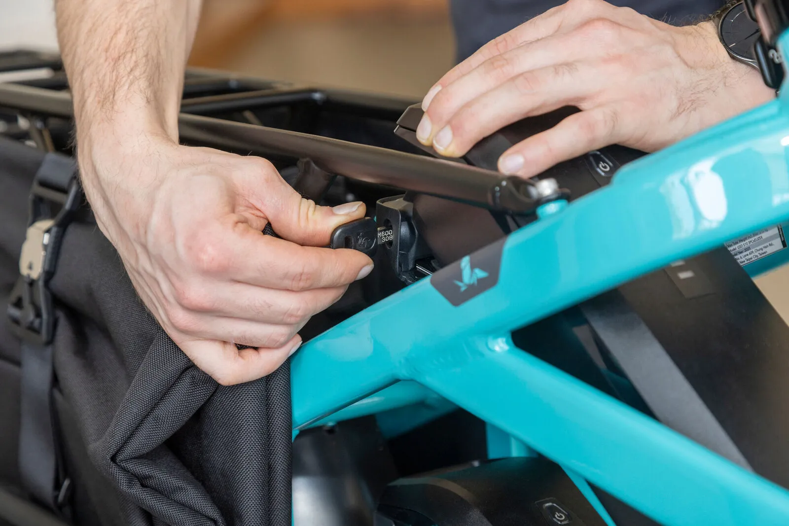 Hands clipping a Cargo Hold pannier onto the rear rack of a beetle blue Tern GSD.
