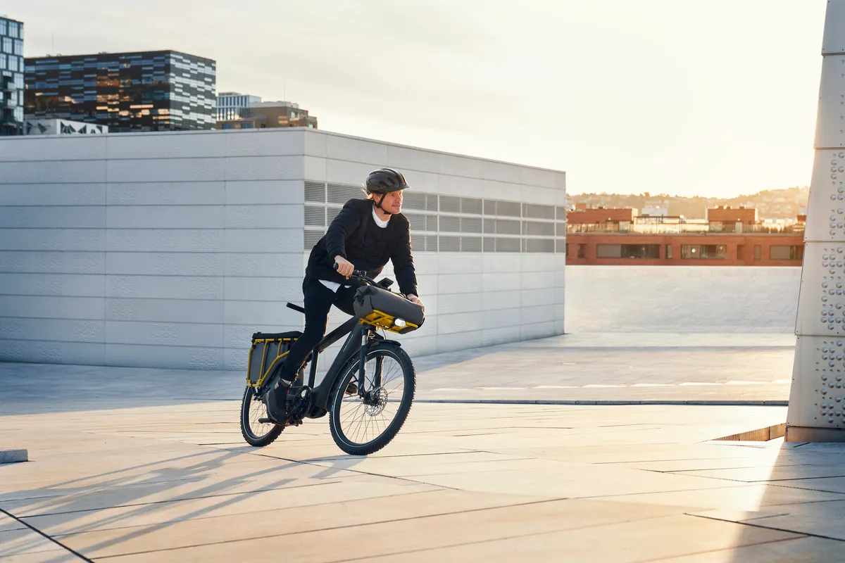Person riding black Multicharger2 on modern urban streetscene at sunset.