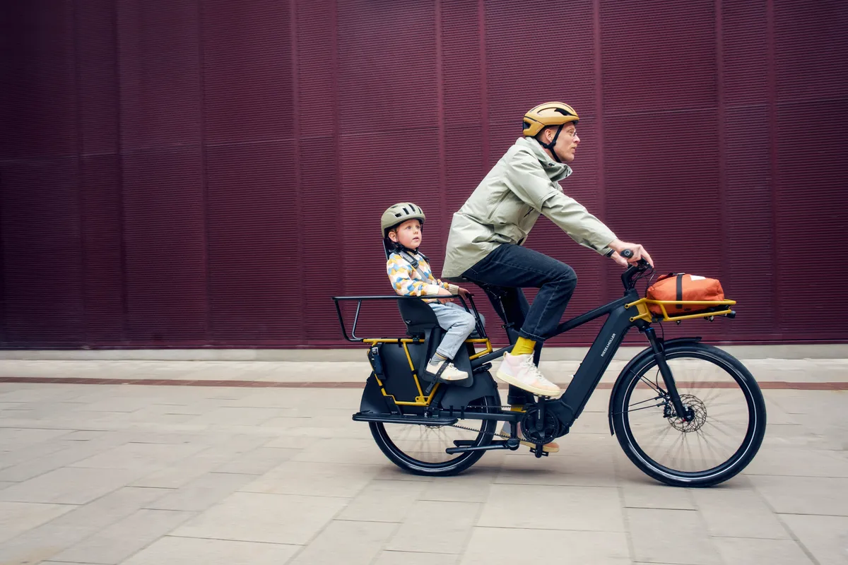 A man riding a Riese & Müller Multicharger2 with a young child in a baby seat on the back.
