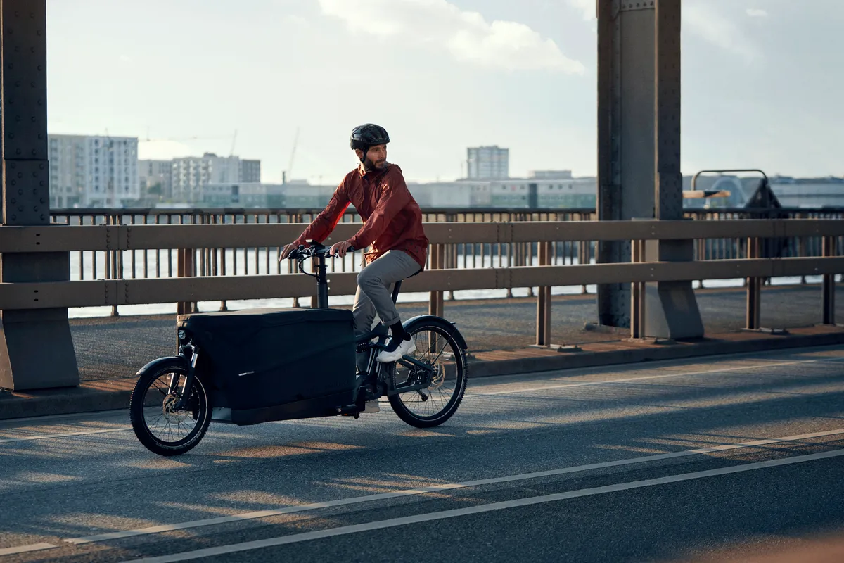 A man riding a Packster 70 Cargo across a bridge in a city.