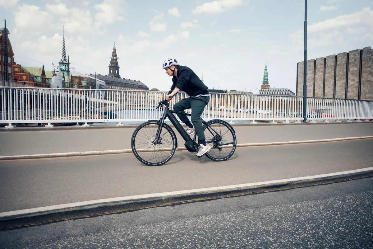 A man riding a black matt Riese & Müller Roadster over a city bridge.
