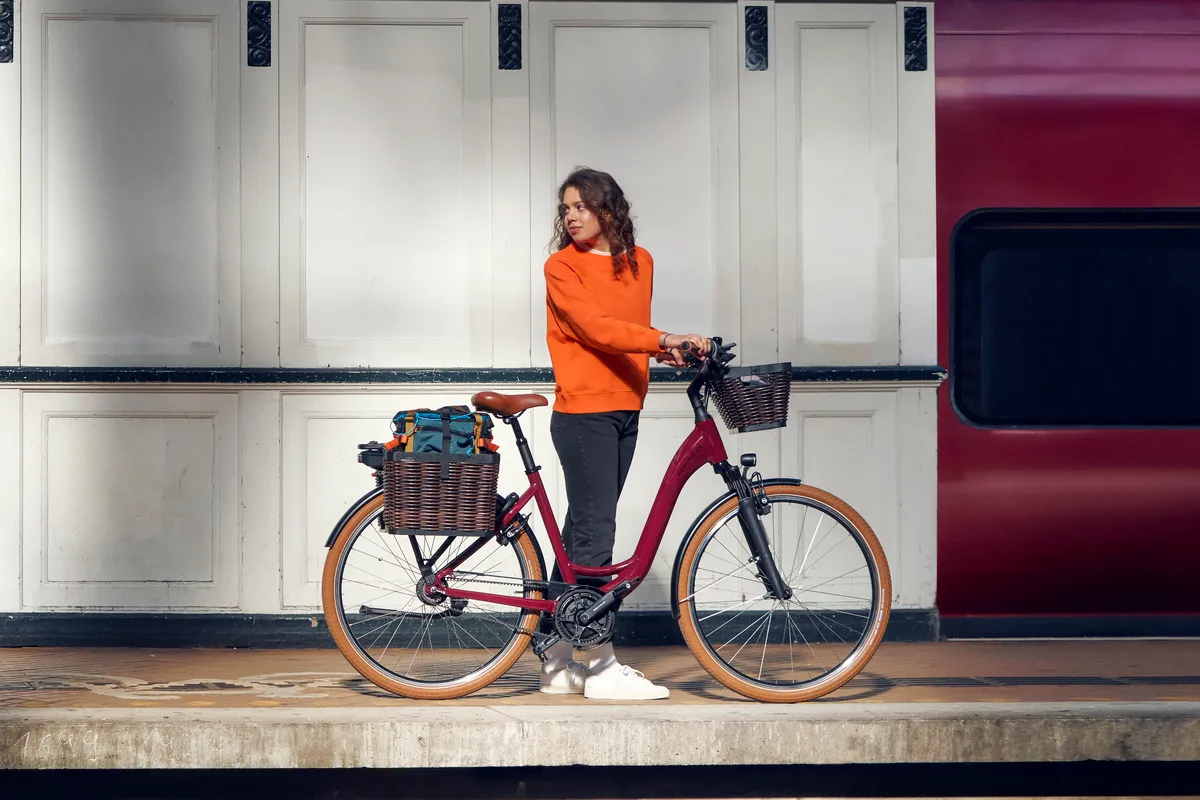 A lady riding a black Nevo bike along a paved street scene.