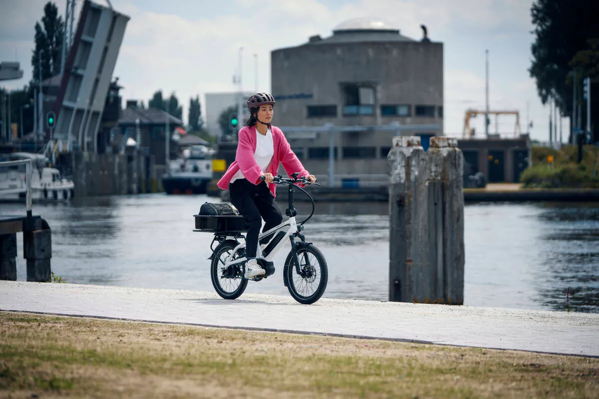 A lady riding a white Tinker along a wharf.