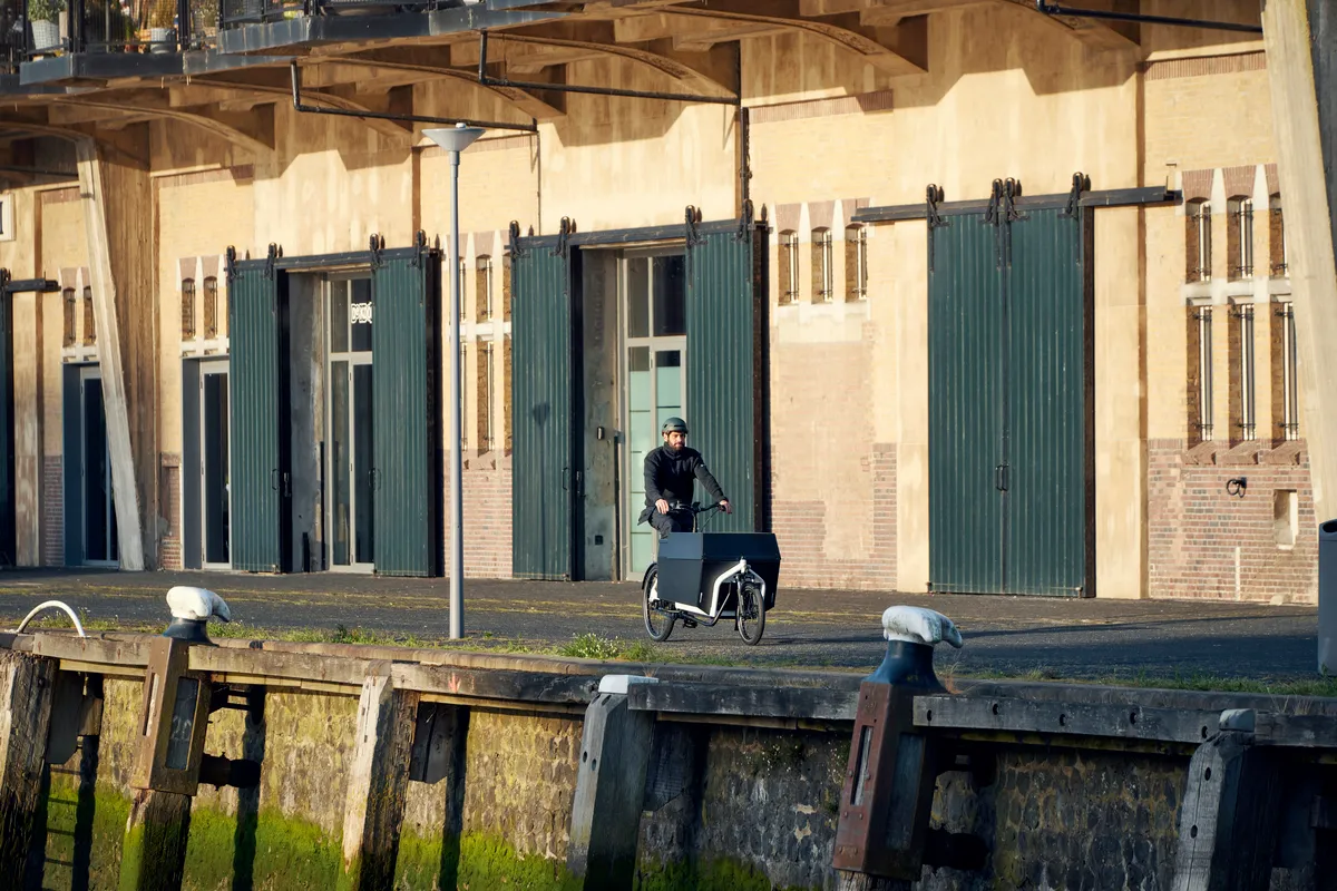 A man riding a Riese & Müller Transporter cargo bike in true white on a city wharf.