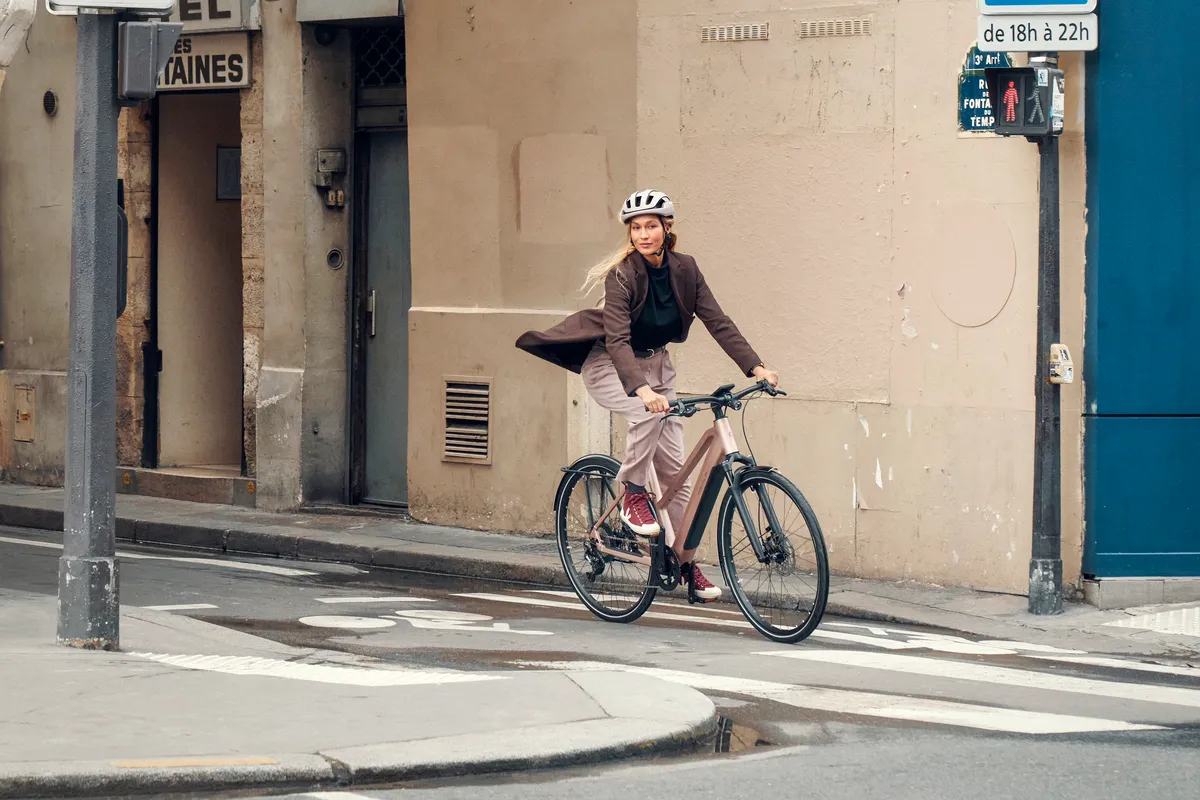 A lady riding a Riese & Müller UBN Seven in rose pink along a street in Paris.